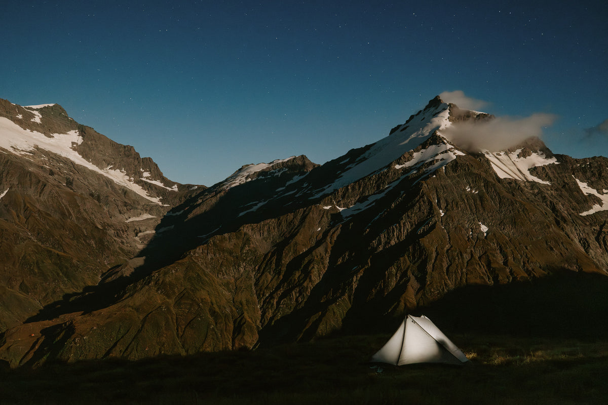 Tent pitched in a mountainous area with snow-capped peaks under a clear night sky.